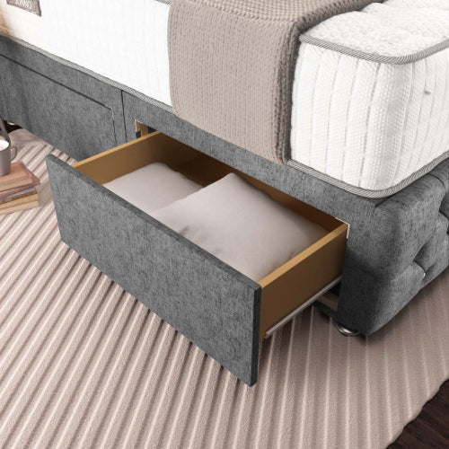 Gray upholstered bed with an open drawer revealing white bedding on a striped carpet.